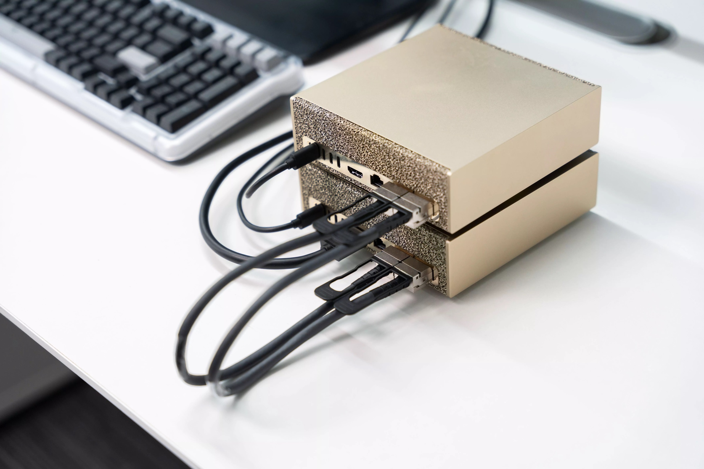Two NVIDIA DGX Spark units stacked on a desk, linked by two QSFP cables, with a keyboard behind them.